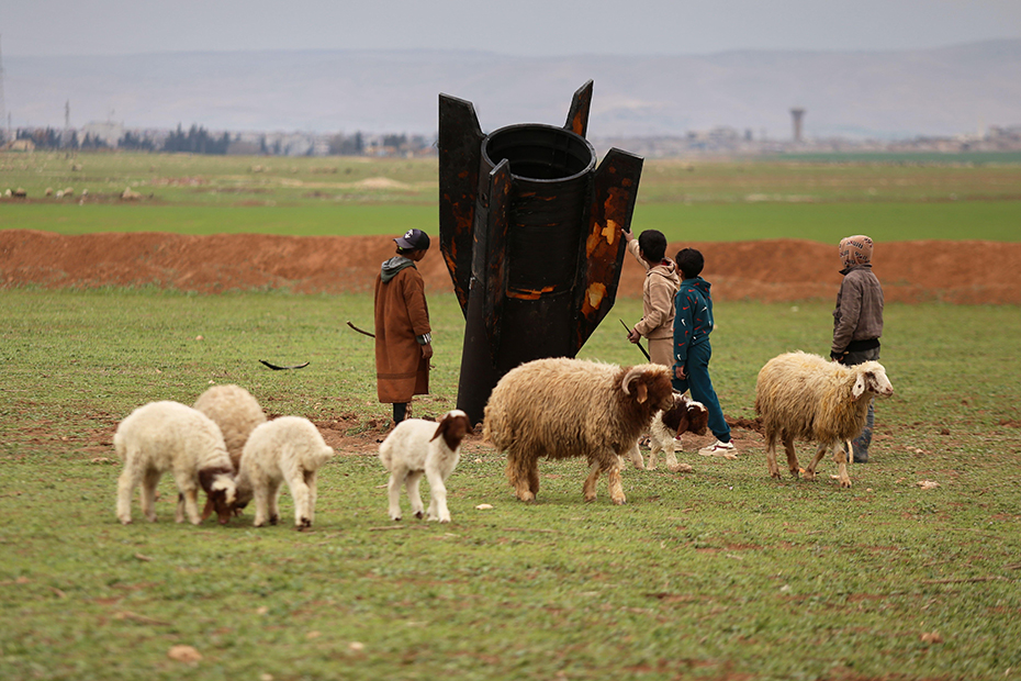 Exposing themselves to the danger of unexploded ordnance, shepherd boys inspect an unexploded Iranian projectile that landed in an open field on the outskirts of Qamishli, eastern Syria