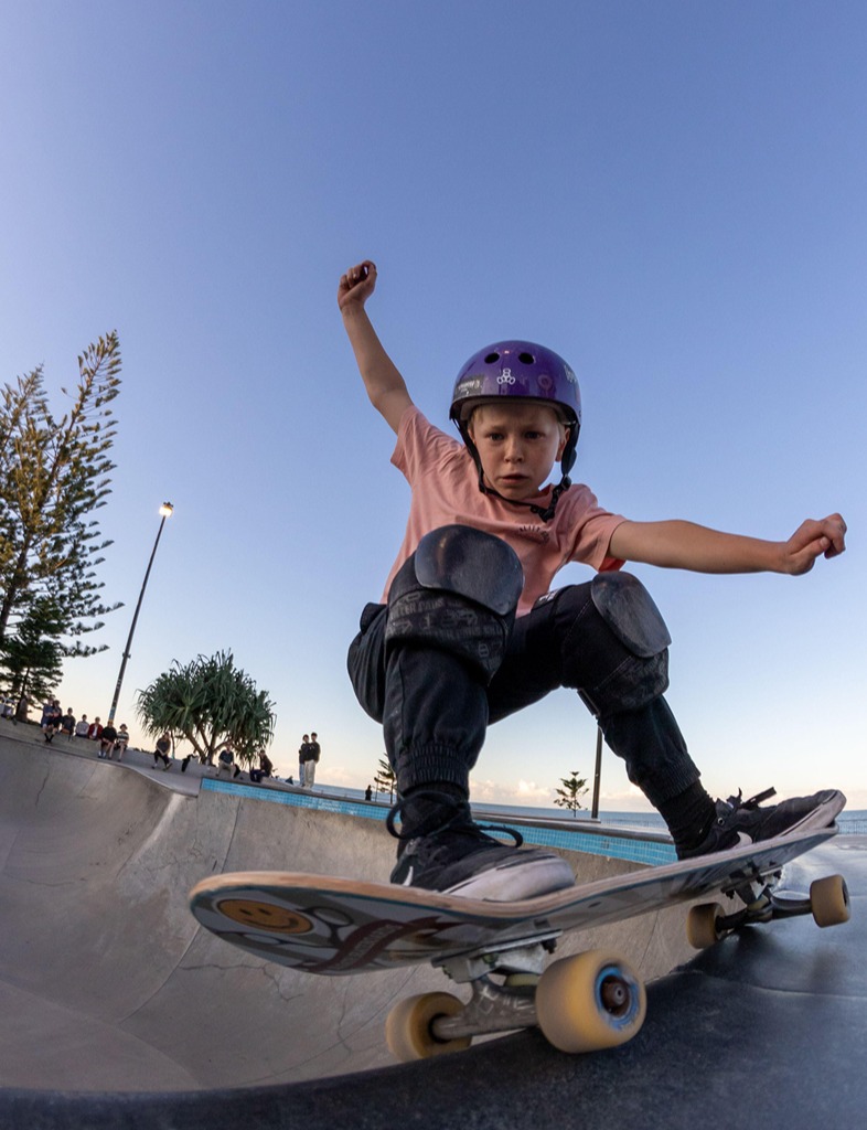 A vertical shot of a kid wearing a helmet doing tricks on a skateboard in a park