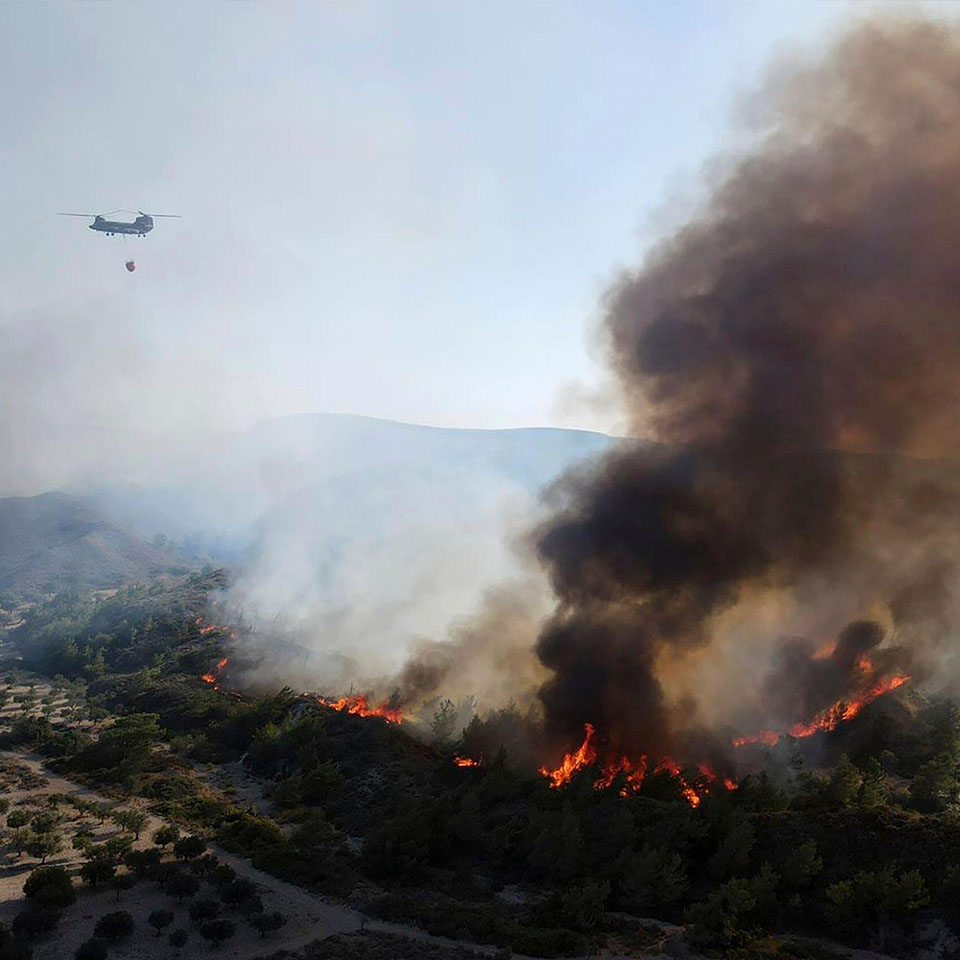 2RE4RJY - A military helicopter operates as flames burn a forest on the mountains near Vati village, on the Aegean Sea island of Rhodes, southeastern Greece.