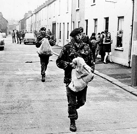 Men of 1st Battalion Welsh Guards carry a bag of gelignite they found in a "bomb factory" they uncovered in a terrace house in the city's Keegan Street during a dawn swoop. 