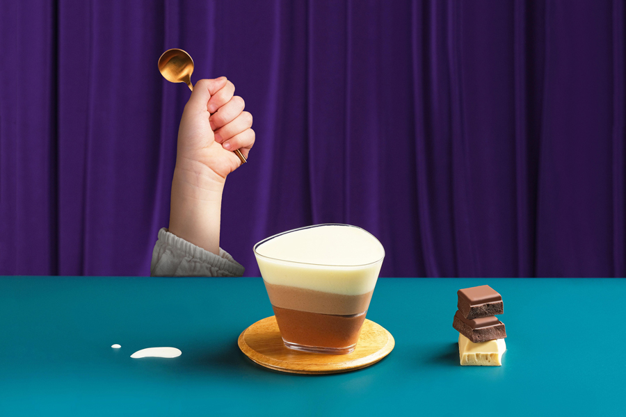 Concetto artistico di caffè con una mano che tiene un cucchiaio e ricchi pezzi di cioccolato accanto a una tazza di cioccolata calda