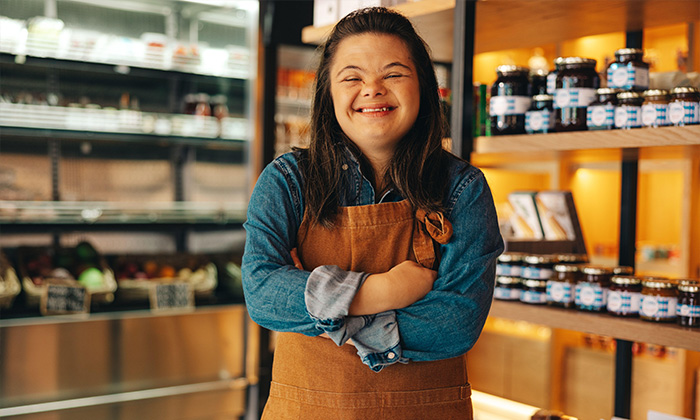 Shop worker with Down syndrome smiling at the camera while standing in a grocery store. Empowered woman with an intellectual disability working in a l