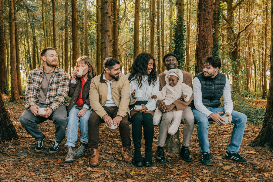 Un gruppo di persone è seduto su un tronco in una foresta. Sono tutti sorridenti e si godono la reciproca compagnia.