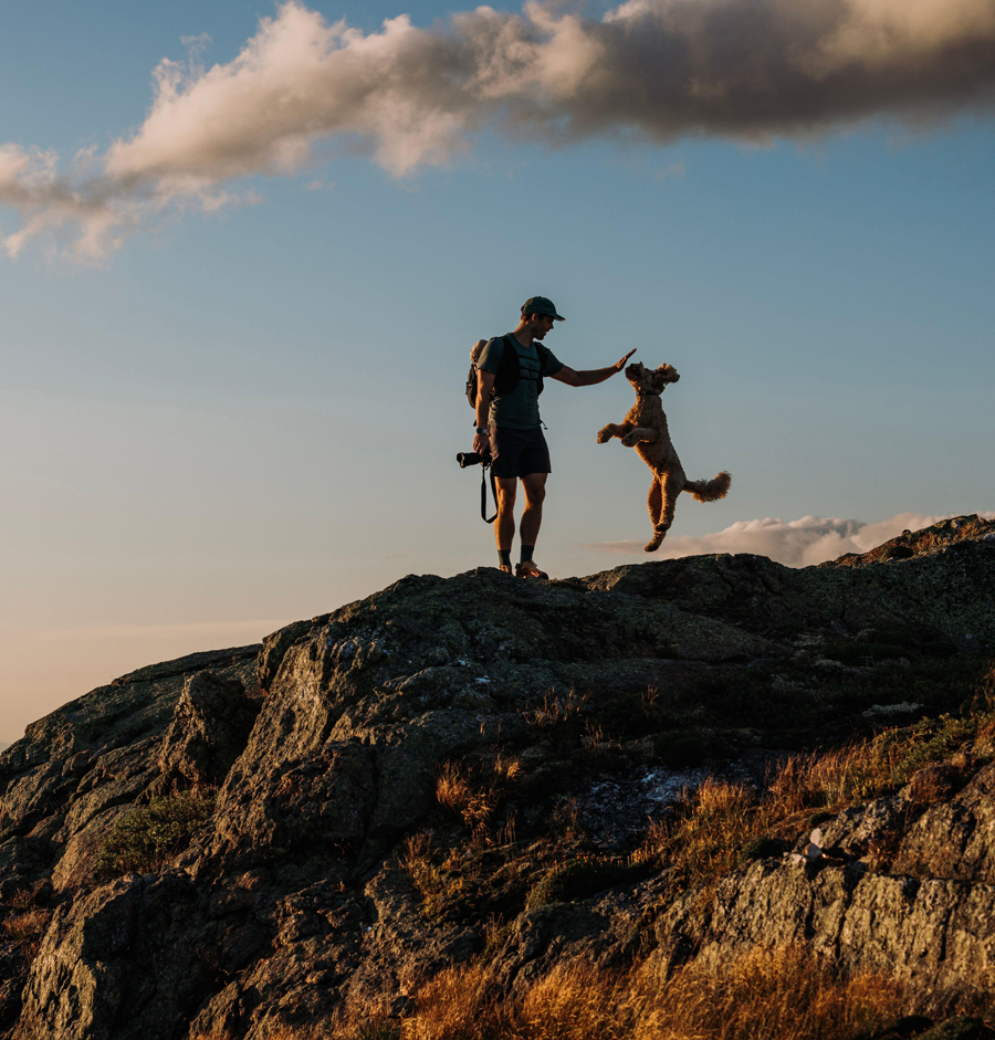 Hiker and his excited jumping dog at sunset in White Mountains, NH