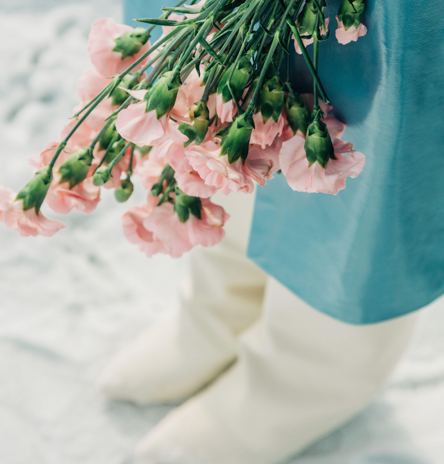 Photo of a person’s lower half holding a bouquet of pink flowers upside down, wearing a blue skirt, against a snowy background