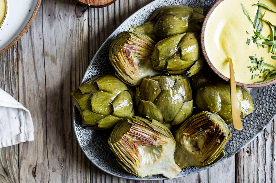 Un piatto di carciofi cotti serviti con una salsa cremosa su un tavolo di legno rustico