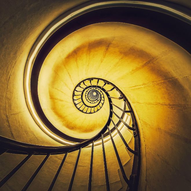 Spiral stairway abstract swirl hypnotising perspective. View downstairs to infinity circular stairs glowing in yellow light background - Image ID: 2PMJFW0 (RF)