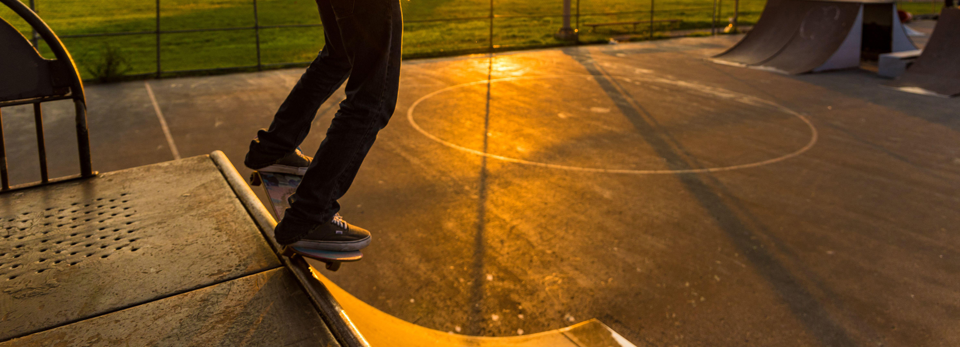 A young man performing skate tricks on a quarter pipe in an urban skate park during golden hour