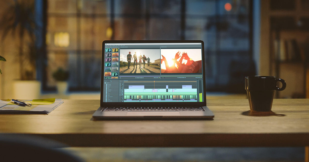 Aufnahme eines Laptop-Computers auf einem Schreibtisch mit professioneller Videomontage-Editing-Software. Im Hintergrund warme Abendbeleuchtung und offener Raum.