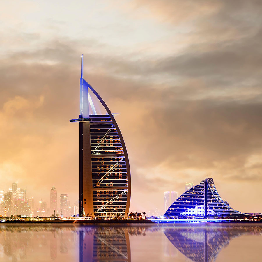 Dramatic sunset over the Dubai skyline with the Burj Khalifa in the distance and the Burj al-Arab luxury hotel in the foreground.