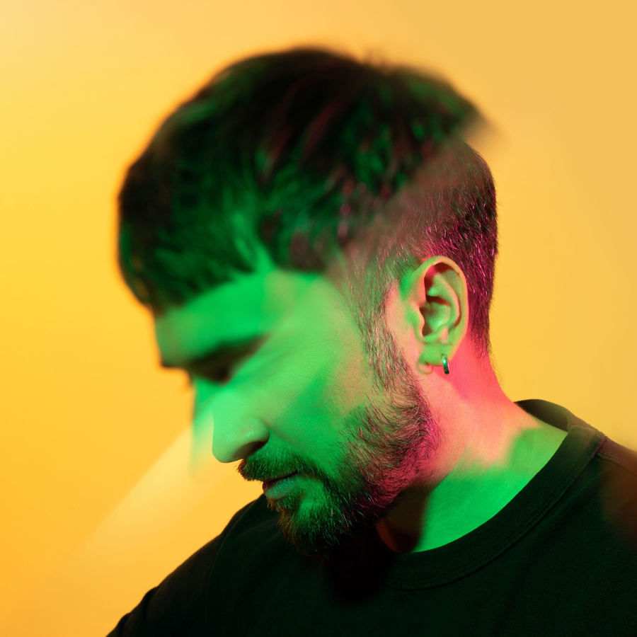 Portrait créatif artistique à travers le prisme d'un homme regardant vers le bas dans des néons verts et roses sur fond jaune.