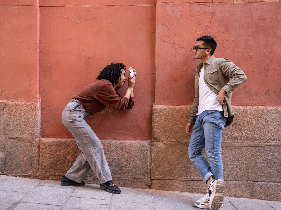 A Chinese man and a Hispanic woman, enjoying a fun photoshoot against a vibrant red wall in Madrid, Spain