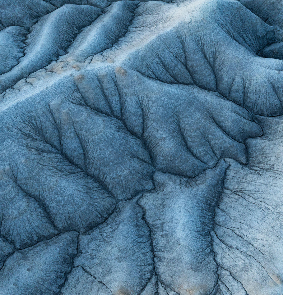 Prise de vue aérienne capturant les textures et les formations complexes des badlands aux teintes bleues, mettant en valeur leur beauté naturelle et leur complexité géologique