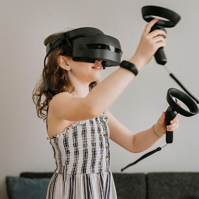 Girl wearing virtual reality simulator playing with joysticks at home.
