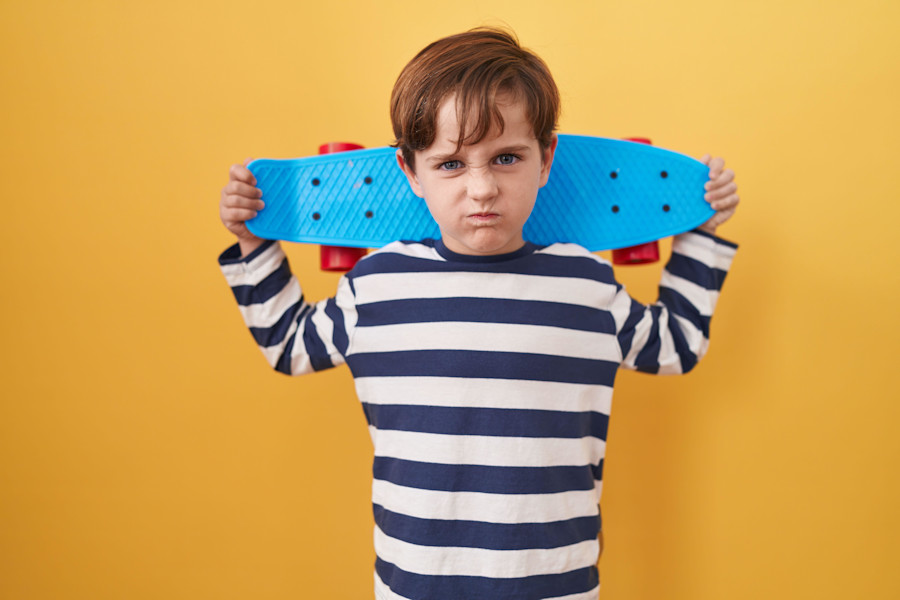 Little caucasian boy holding skate over yellow background skeptic and nervous, frowning upset because of problem. negative person.