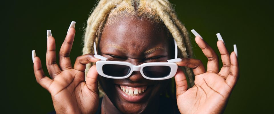 Portrait of cheerful black woman holding sunglasses in front of face - Image ID: 2R262MF (RF)