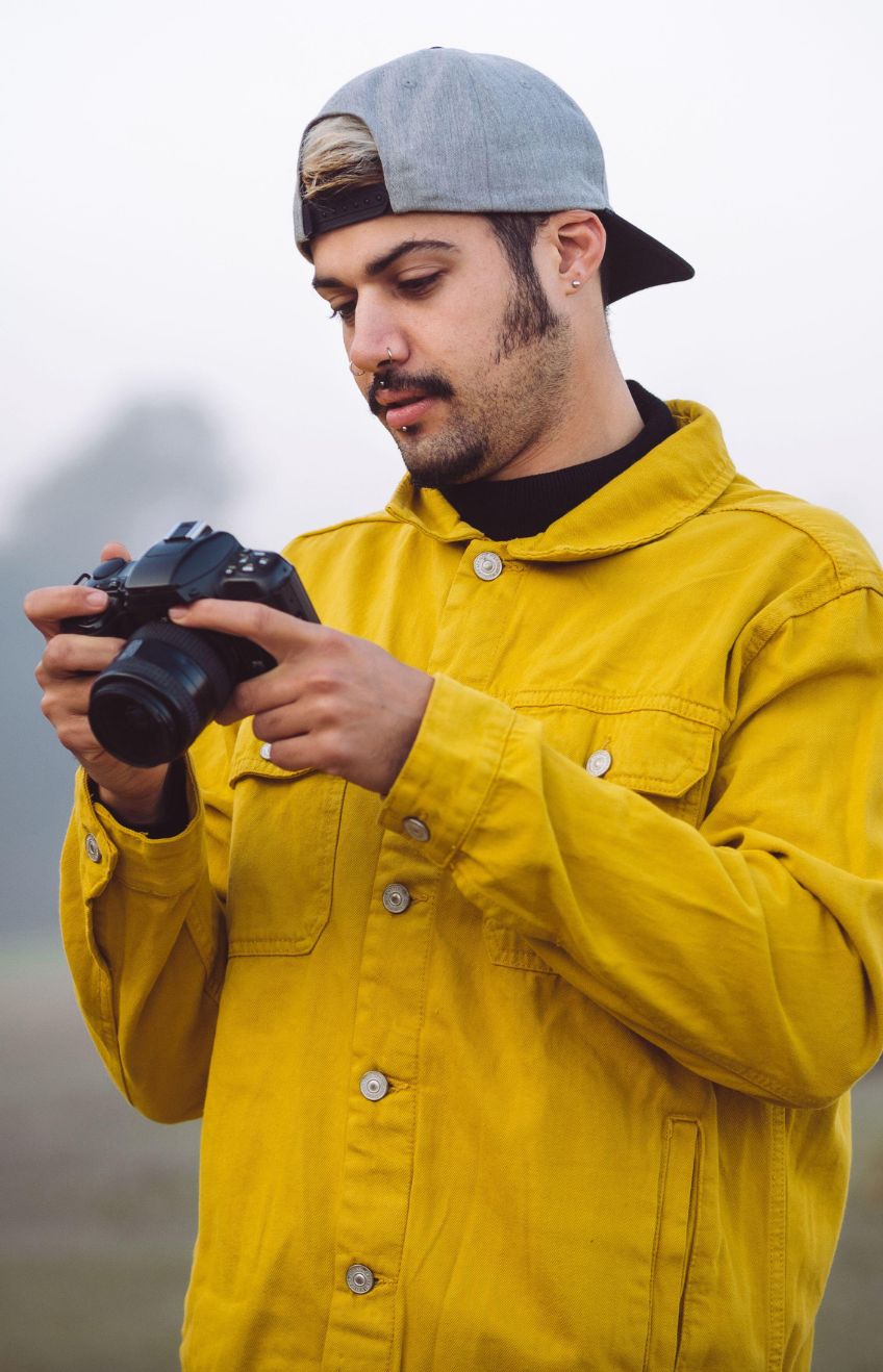 Young male photographer in yellow denim jacket taking photo on photo camera while standing on foggy blurred nature background