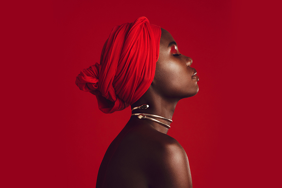 Side view of a woman with red turban in studio. Stylish female model with her eyes closed against red background