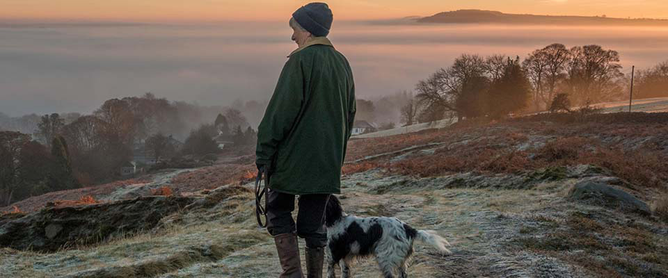 Femme promenant son chien sur un chemin sur Ilkley Moor par une matinée givrée, admirant les vues de la campagne et l'inversion de nuages dans la vallée de Wharfe, Yorkshire, Royaume-Uni.