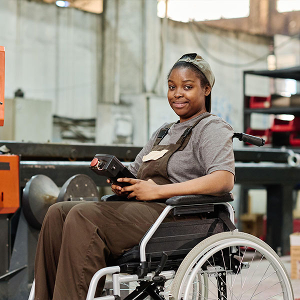 Portrait of African worker sitting in wheelchair with remote control to control the operation of machine at factory