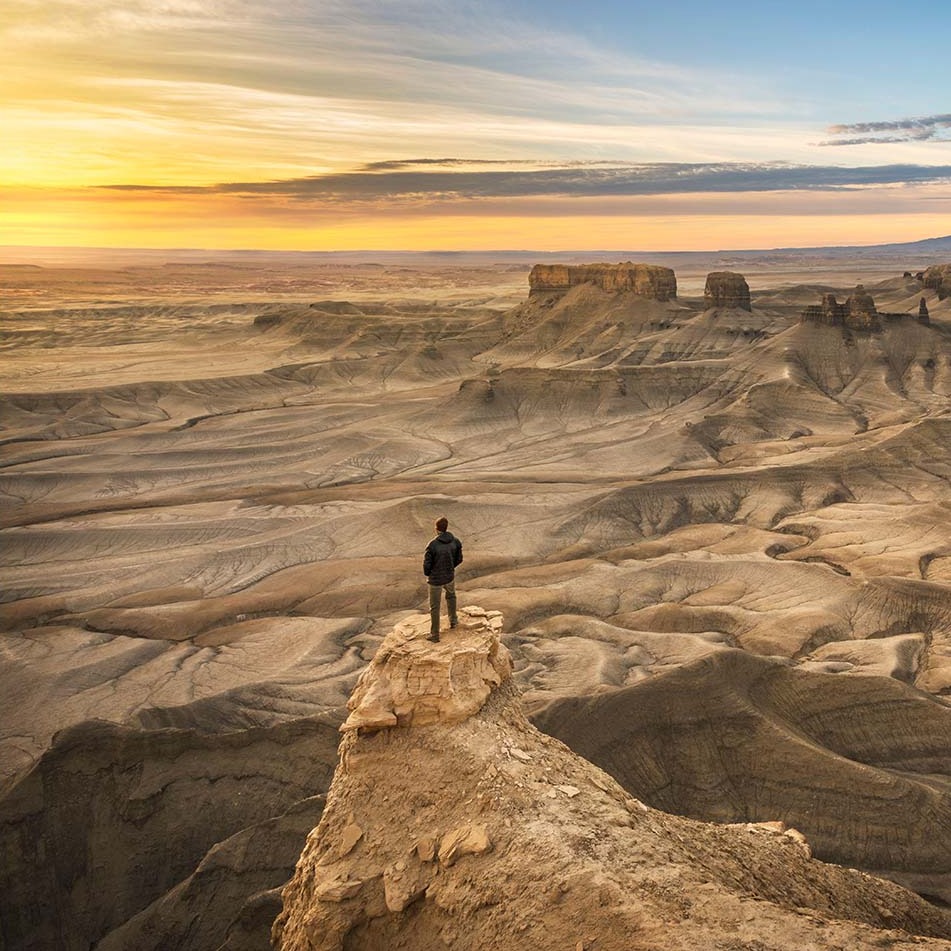 One person standing on rock outcrop in a dramatic desert landscape. 
