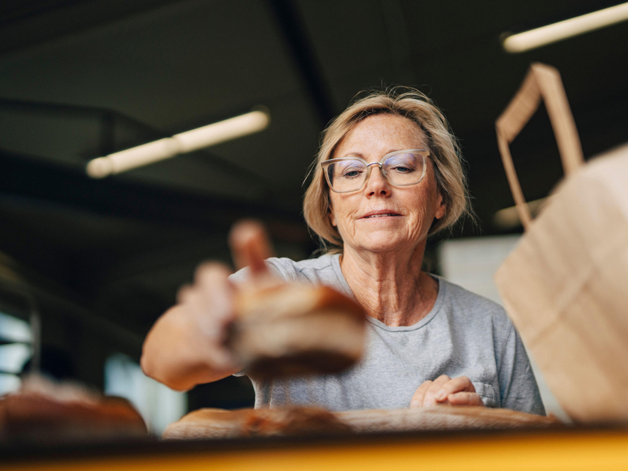 Low angle view of senior female baker arranging cinnamon bun for sale while working at bakery