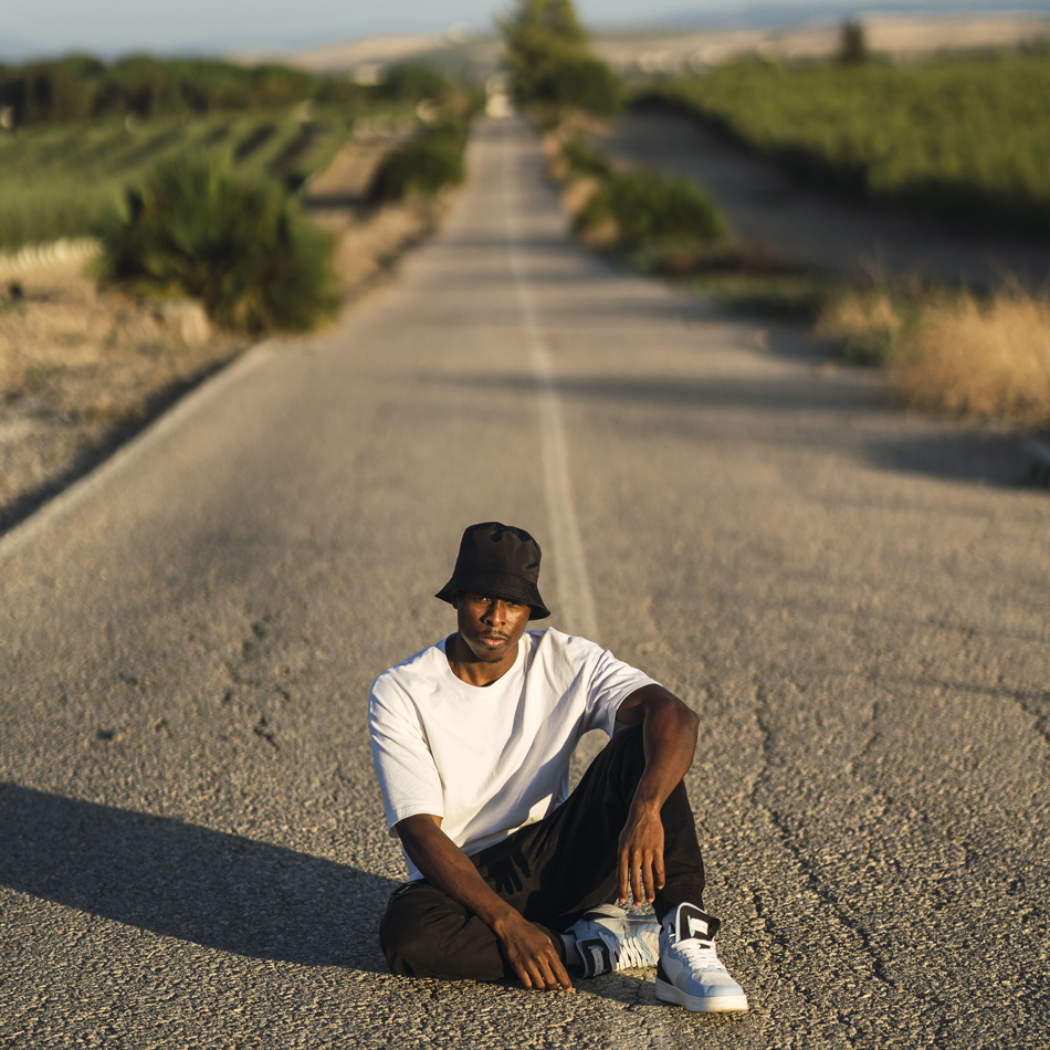 Vertical shot of a young cool black male in a street style outfit posing sitting on a rural road