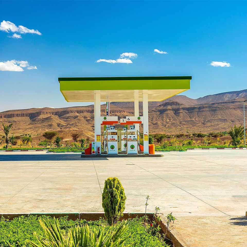 Stazione di servizio di colore verde in una zona arida del deserto, sullo sfondo la catena montuosa dell'Atlante in Marocco.