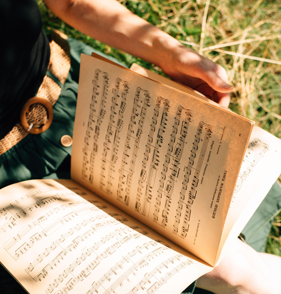 Detailaufnahme einer Person, die ein aufgeschlagenes Buch in der Hand hält, dessen Seiten mit Notenzeichen bedeckt sind