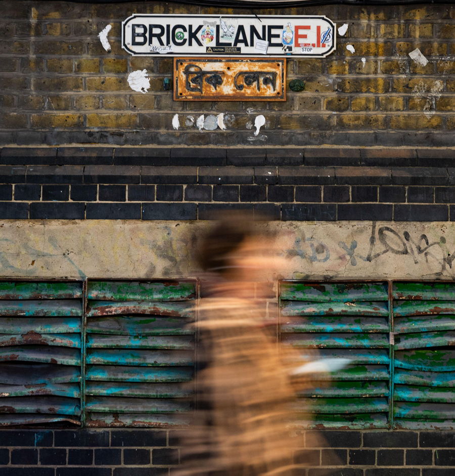 Blur of person walking past Brick Lane sign in London